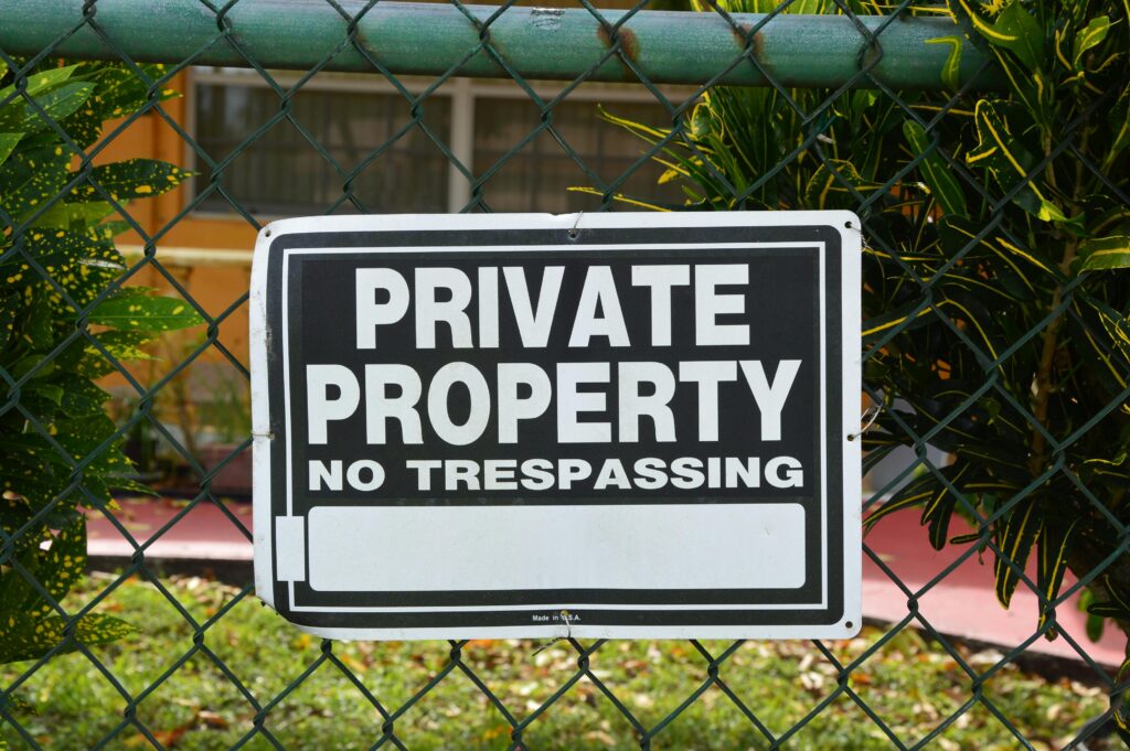 Close-up of a private property no trespassing sign on a chain-link fence with greenery in the background.